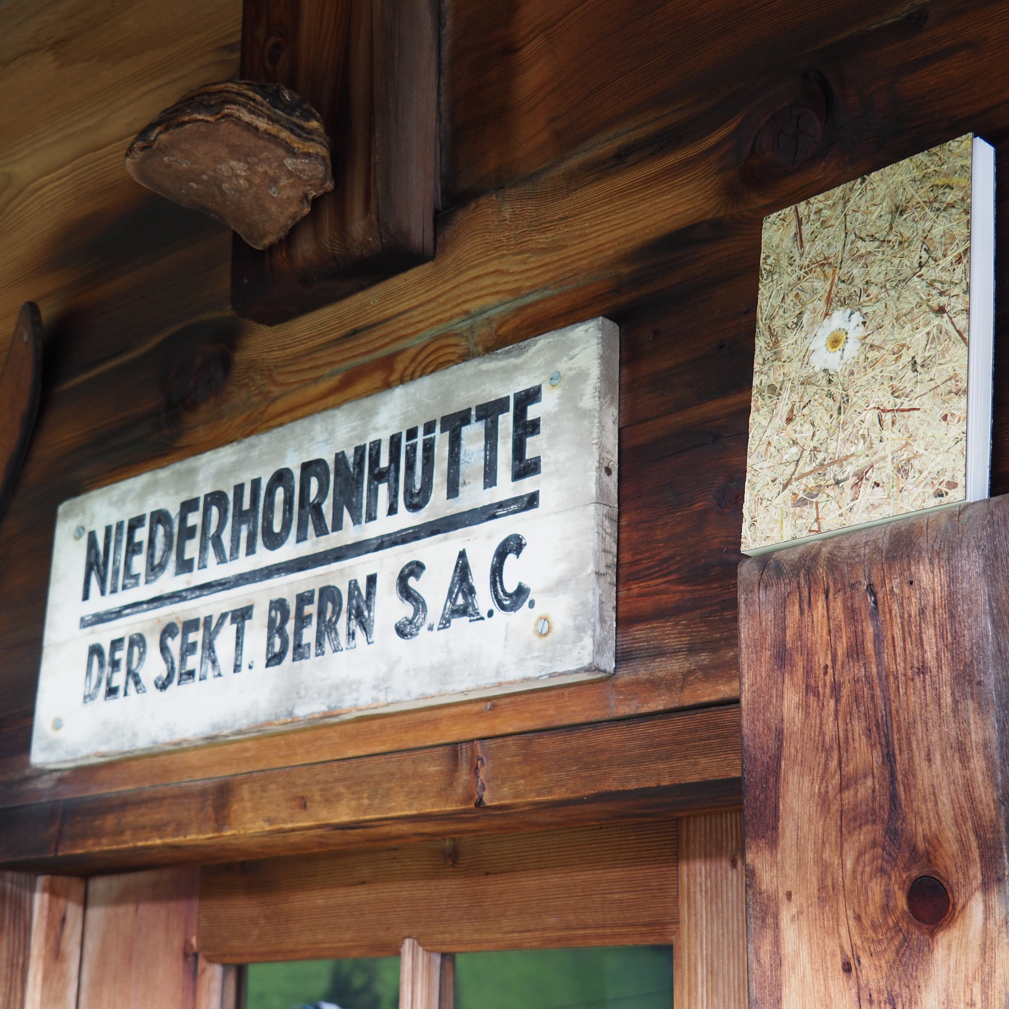 Notizbich Handggebunden mit Heu und einer Marguerite Aufgenommen neben dem Plakat der Niderhornhütte SAC